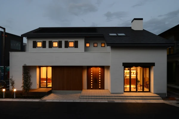 夕暮れに窓から明かりがもれる住宅の外観